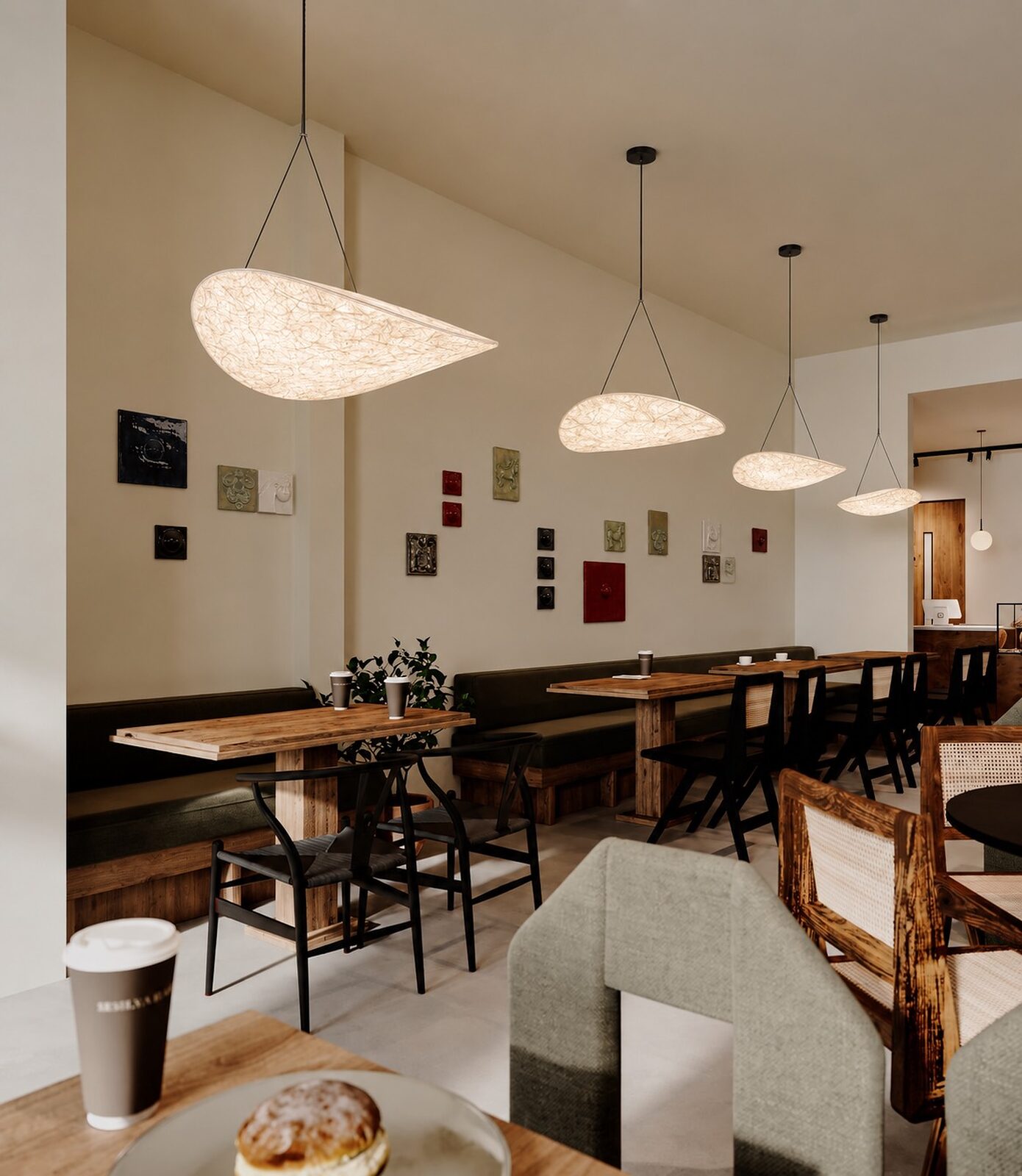 Banquette seating beneath leaf-shaped paper pendants and the handcrafted wall tiles, with coffee and a pastry on the table