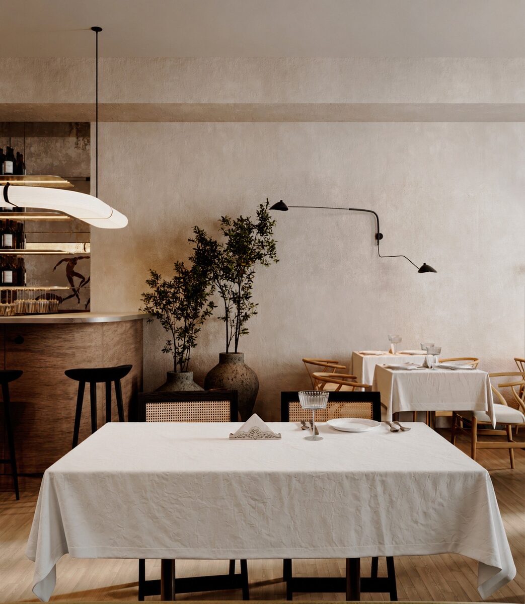 A white-clothed table beside an olive tree, lit by slim black wall lights
