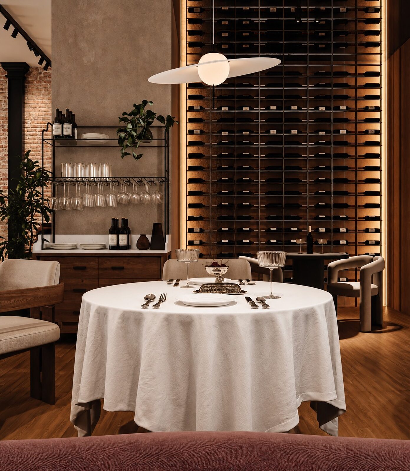 A round table dressed in white linen in front of the full-height backlit wine wall